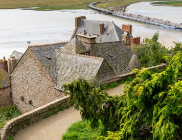 Top view of a stone building, with a dirt road and a large lake in the background
