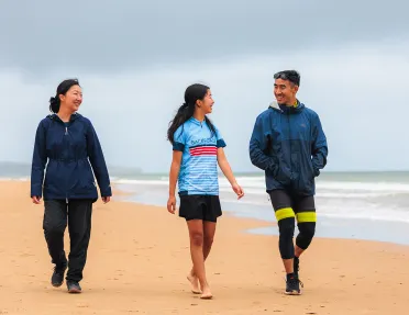 Two women and one man smiling while walking on a beach