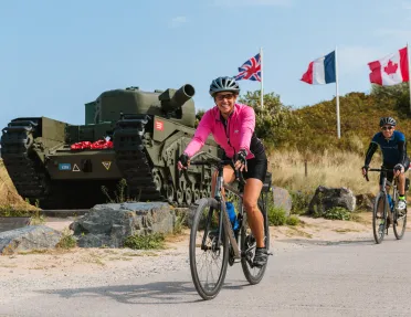 Woman in pink, biking in front of a green tank with flags waiving in the background