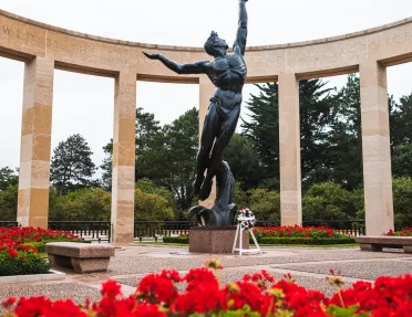 Stone statue on a man in the middle of a garden of red flowers