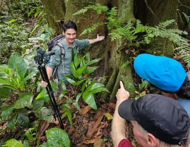 Man holding tripod wile pointing to a large tree