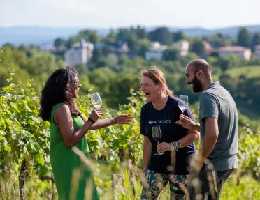 Two women and one man standing in a vineyard while holding glasses of wine