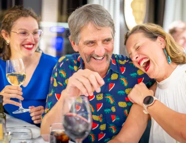 One man and two women, smiling and laughing while holding wine glasses