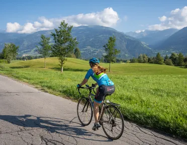 Woman riding a bike on an empty road, with a large valley to the right
