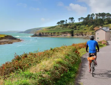 Man in a blue jersey, riding a bike on a road along a large lake