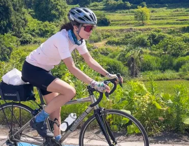 Woman riding bike on a path with large forest in the back
