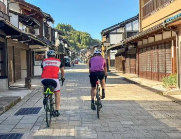 Two men biking on a stone road in the middle of a Japanese town
