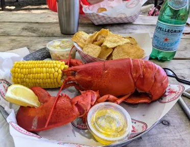 Plate with a boiled lobster, a half of corn and a plate of chips