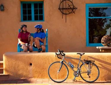 Two women sitting in front of an orange house, with a bike parked out front