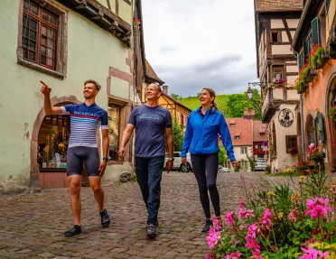 Two men and one woman walking on a stone alleyway, pointing and smiling