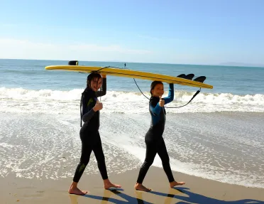 Two girls carrying a yellow surfboard over their head