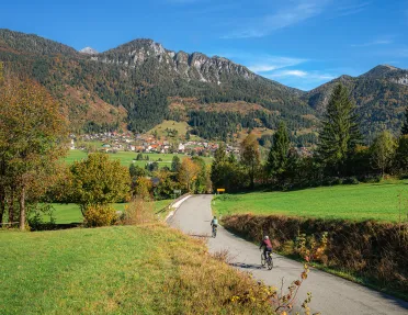 Two bikers on a road going towards a town and large mountains