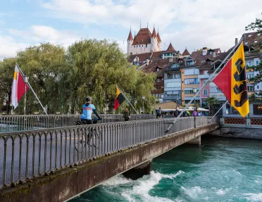 Woman biking across a bridge surrounded by large flags