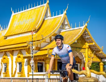 Man smiling while biking in front of a white and gold temple