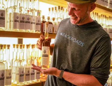 Man smiling while holding up a skinny bottle of alcohol