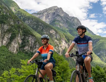 Two women smiling while riding bikes with tall mountains in the background