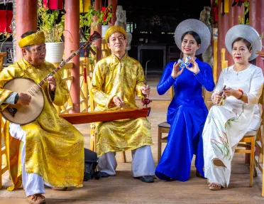 Two men and two women wearing traditional Vietnamese attire while playing instruments