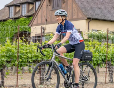 Woman wearing biking gear and riding a bike in front of a wooden home