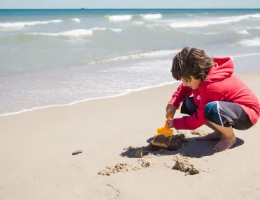Boy on the beach, playing with the sand and a scooper
