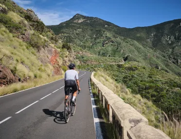 Person riding their bike on a road with large, grassy mountains in the distance
