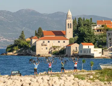 Group of people holding bikes over their heads, with a town and ocean in the background