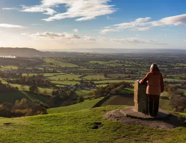 Woman on top of a hill with a stone pillar looking out to a large valley