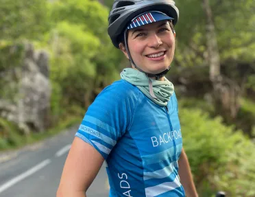 Woman wearing a Backroads jersey and helmet, with a road surrounded by trees in the background