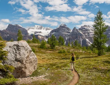 Woman walking along a dirt trail with large mountains in the distance