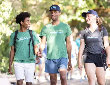 Two men and one woman walking on a trail with blurry trees in the background