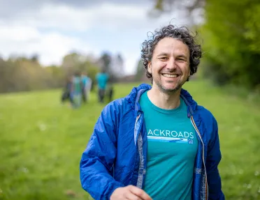 Man wearing a Backroads branded shirt, smiling with a blurry grass field behind him