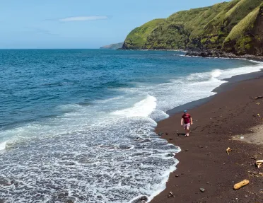 Man walking on a beach, with grassy mountains in the background