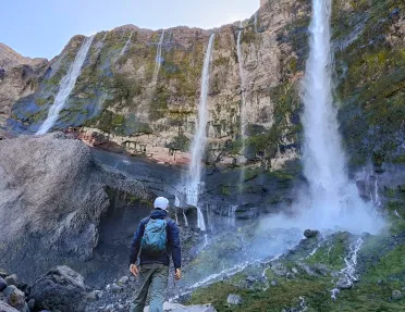 Hiker looking up at a tall cliff with multiple, active waterfalls