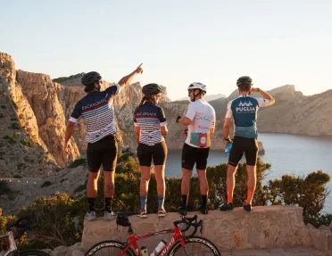 Group of people wearing biking gear, standing on a ledge looking out to a lake