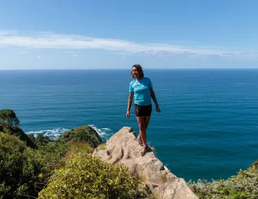 Woman standing on a boulder with the ocean in the distance