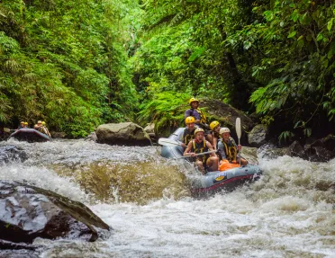 Group of people smiling while paddling on a raft through a river