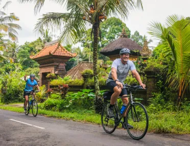 Man and woman biking on a road with jungle in the background