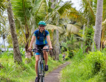 Woman smiling while riding a bike through a road surrounded by palm trees