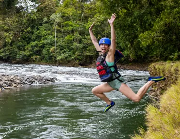 Woman wearing a helmet and life vest jumping into a lake