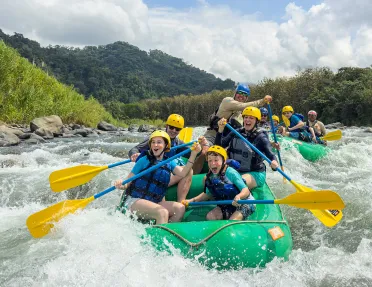 Two groups of families on green rafts, paddling in a river