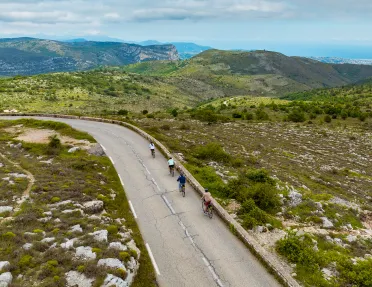 Group of people biking on an empty road, surrounded by a grassy valley