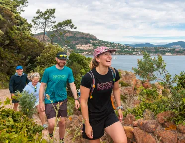 Group of people smiling while hiking on a trail with the ocean in the background