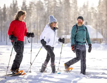 Women and two men with hiking poles and snow shoes, walking in a valley of snow