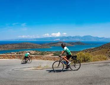 Two people riding bikes down a road, with a large lake in the distance