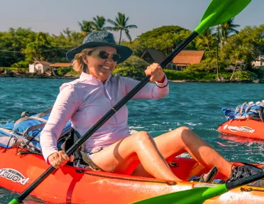 Woman wearing a hat and sunglasses, paddling on an orange kayak