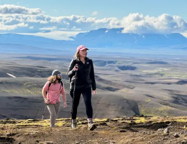 Man and woman ascending a dirt trail with large hills in the background