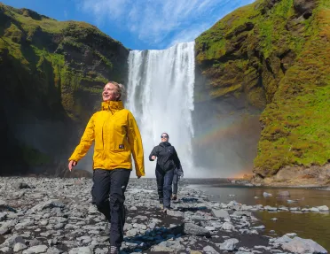 Two women smiling while walking on a rocky path in front of a waterfall