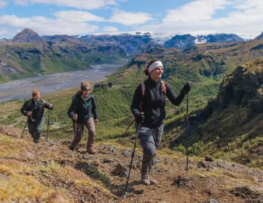 Group of three people with hiking poles, walking on a dirt and gravel trail on a hill