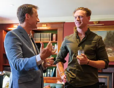 Two men holding alcohol and smiling, with a library in the background