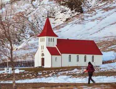 Person walking on a dirt path with a red and white church in the background