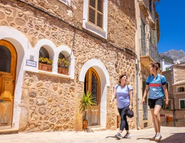 Two women smiling while walking through an alleyway and stone buildings surrounding them